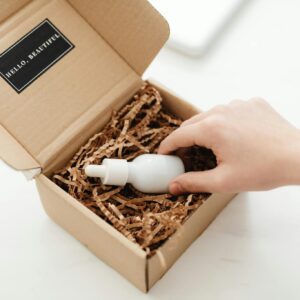 A hand unboxes a beauty product in a sustainable cardboard package with shredded paper.