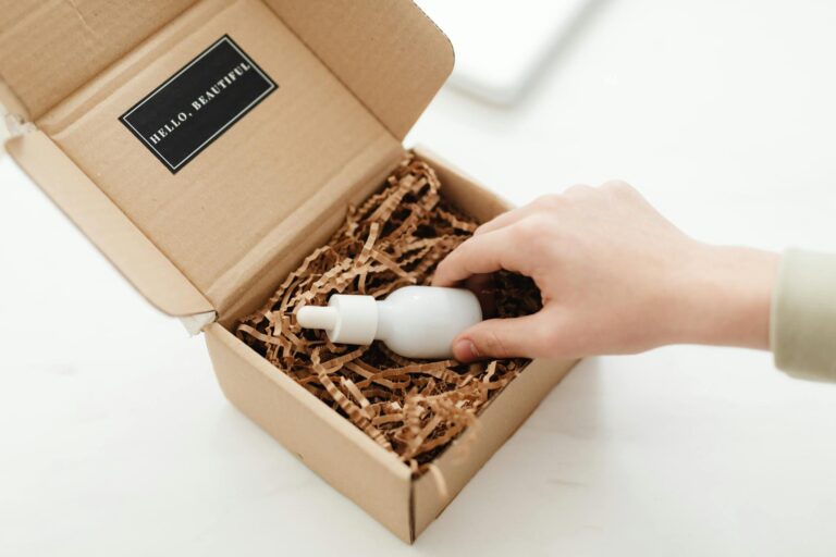 A hand unboxes a beauty product in a sustainable cardboard package with shredded paper.