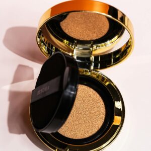 Open golden compact foundation on a white background showcasing makeup elegance.