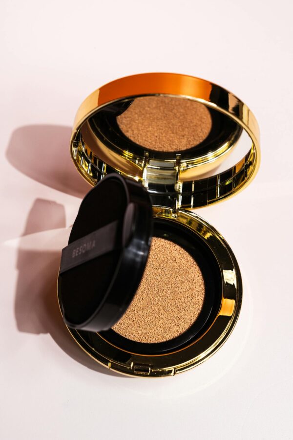 Open golden compact foundation on a white background showcasing makeup elegance.